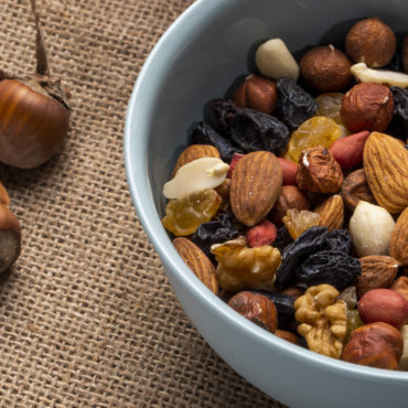 side view of mix of nuts and dried fruits in a bowl on rustic background